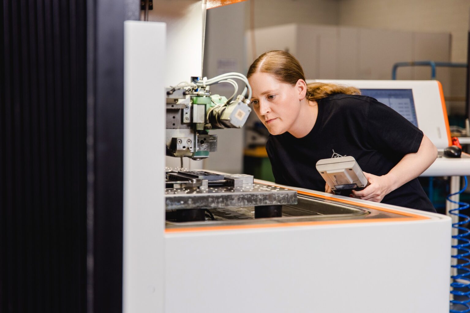 Eine Frau, die eine CNC- oder Präzisionsfertigungsmaschine genau inspiziert, während sie ein Kontrollgerät hält