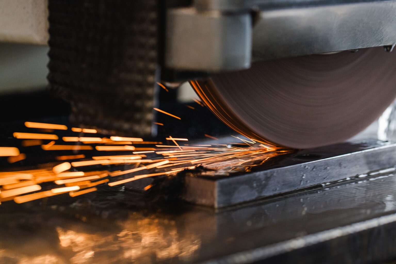 Nahaufnahme einer Schleifmaschine in Betrieb, die leuchtend orangefarbene Funken sprüht, während sie ein Metallwerkstück schneidet oder formt.